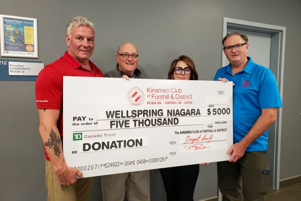 Four People including Kevin Coyle standing in the hallway of the Meridian Community Centre
holding a large novelty donation check to Wellspring for $5,000.